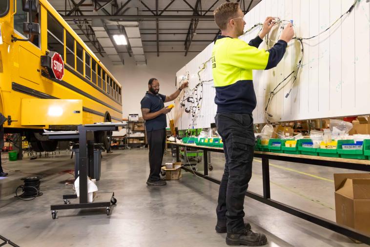Two technicians assemble a wiring harness for a school bus repower. 